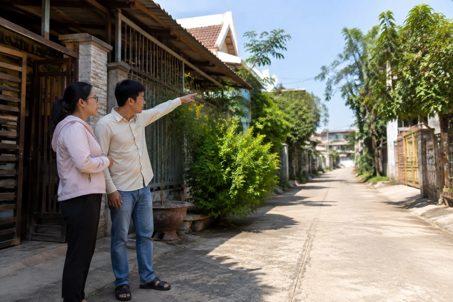 Hai người đứng trước một ngôi nhà dân cư tại khu phố Gia Nghĩa, một người chỉ tay về phía đường vào và hàng xóm xung quanh trong khi người kia quan sát, thể hiện bước kiểm tra thực