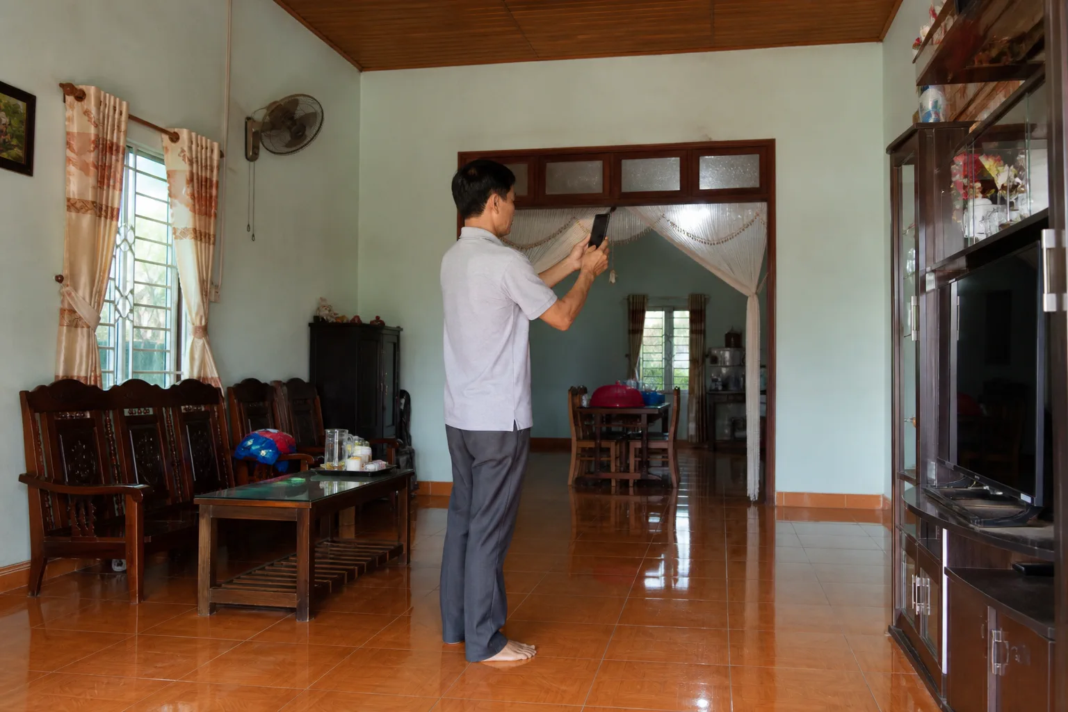 Chủ nhà tại Gia Nghĩa chuẩn bị thông tin tài sản từ xa trong không gian nhà ở thực tế, kiểm tra các góc phòng và ghi nhận tình trạng căn nhà bằng điện thoại trước khi đăng tin.