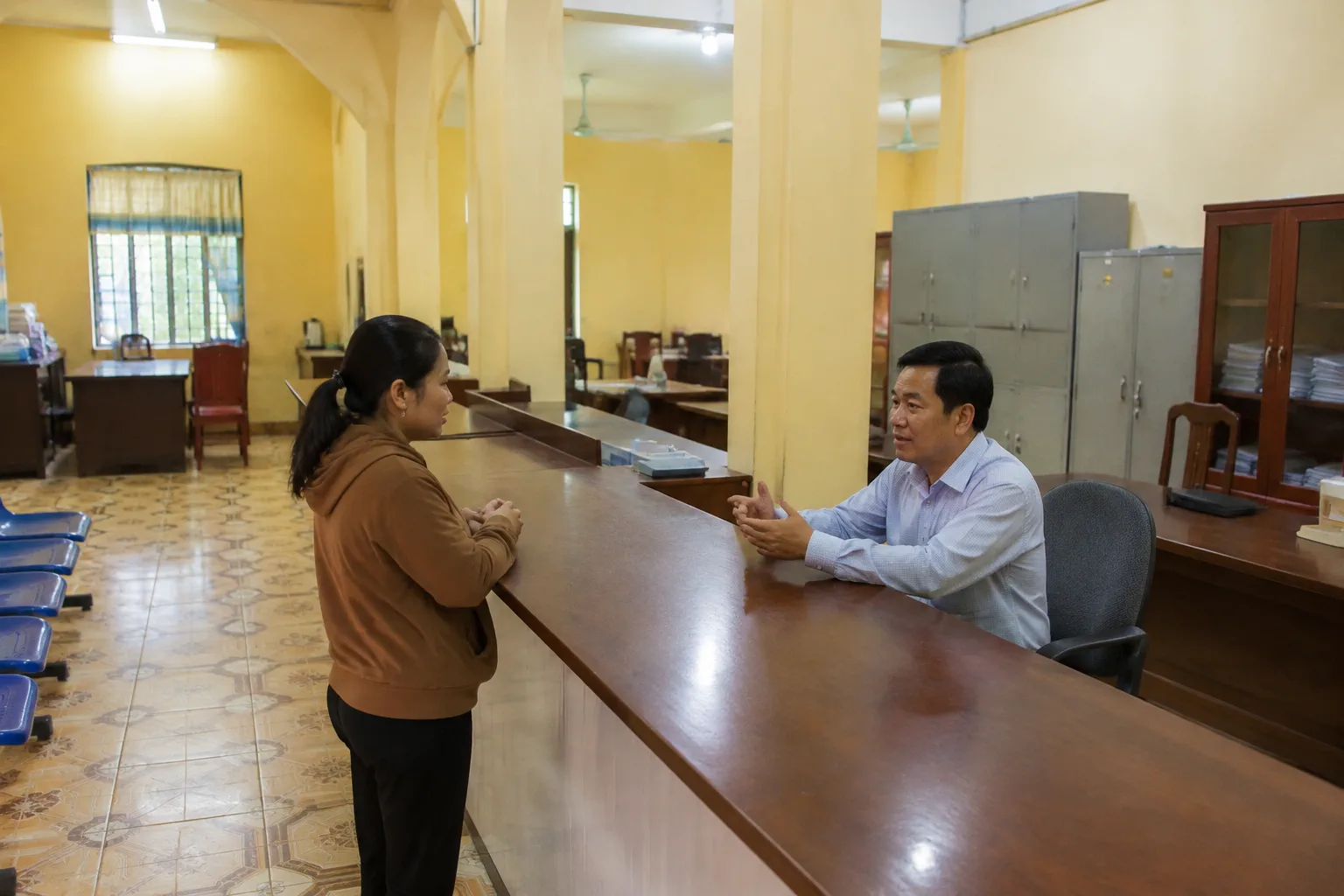 Nhân viên văn phòng địa phương hướng dẫn người dân tại quầy tiếp nhận hồ sơ của một cơ quan hành chính tỉnh Đắk Nông, thể hiện bước xác minh thông tin chính thức khi cần hỗ trợ ngo