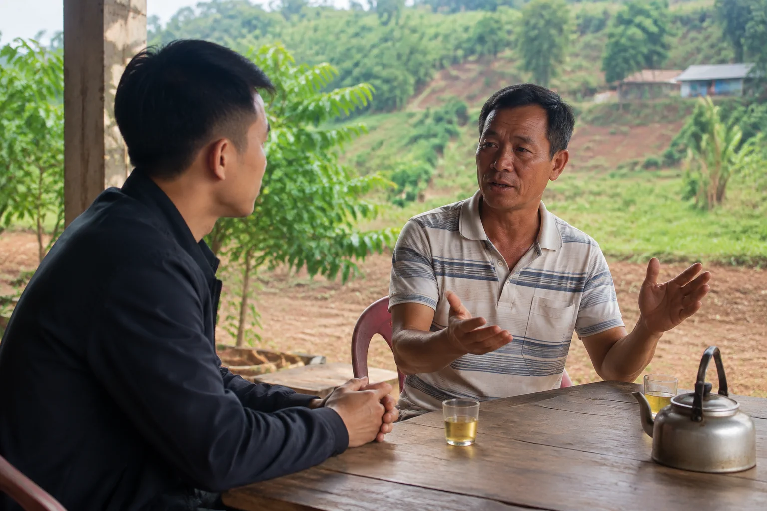 Hai người đang trao đổi về kế hoạch giao dịch tại một không gian ngoài trời yên tĩnh ở Đắk Nông, tập trung vào việc đặt câu hỏi và làm rõ thông tin trước khi ký thỏa thuận.