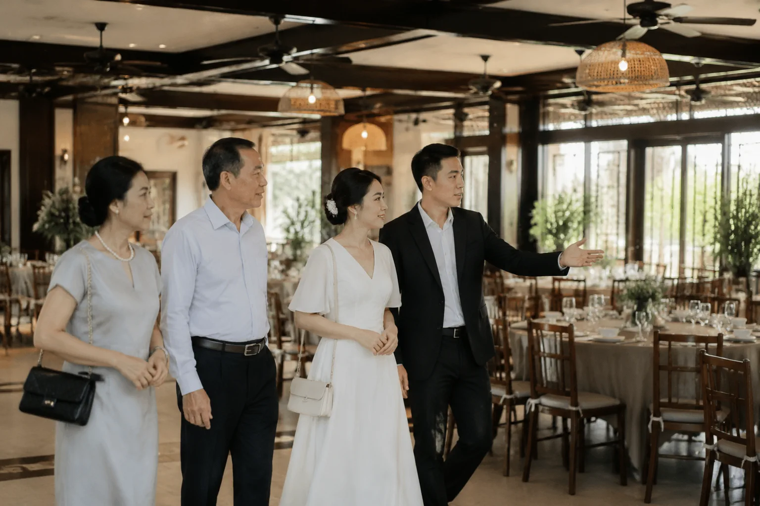Cô dâu chú rể người Việt cùng gia đình quan sát không gian sảnh tiệc cưới tại nhà hàng trước khi trao đổi kế hoạch tổ chức, thể hiện quá trình đánh giá địa điểm theo phong cách buổ