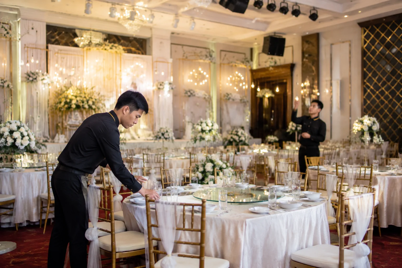 Nhân viên nhà hàng Việt Nam kiểm tra khu vực bàn tiệc và các chi tiết trang trí trong sảnh cưới trước giờ đón khách, thể hiện sự phối hợp các hạng mục không gian và kỹ thuật trong