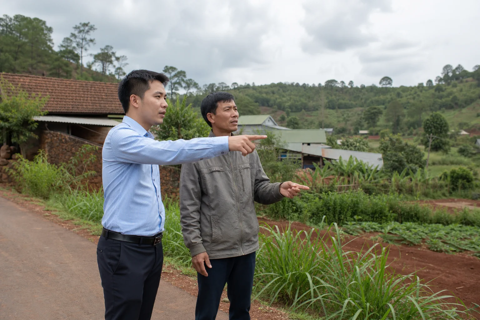 Người mua bất động sản tại Đắk Nông cùng một người hỗ trợ trao đổi kế hoạch khảo sát khu vực tại một không gian ngoài trời gần khu dân cư, tập trung vào việc chuẩn bị câu hỏi trước