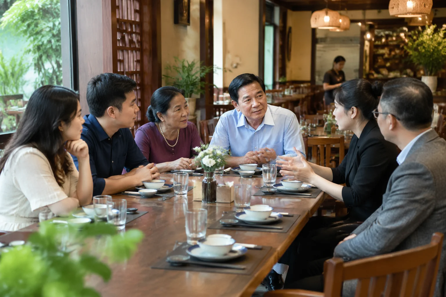 Một nhóm khách Việt Nam nhiều độ tuổi đang cùng trao đổi kế hoạch cho buổi gặp mặt bên bàn ăn đã chuẩn bị một phần trong nhà hàng, thể hiện việc xác định mục đích và yêu cầu riêng