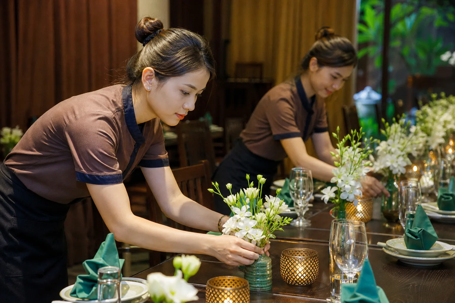 Nhân viên nhà hàng Việt Nam đang kiểm tra cách bố trí khu vực trang trí sự kiện với hoa, bàn tiệc và các chi tiết decor đã sắp xếp, thể hiện quá trình hoàn thiện không gian trước g