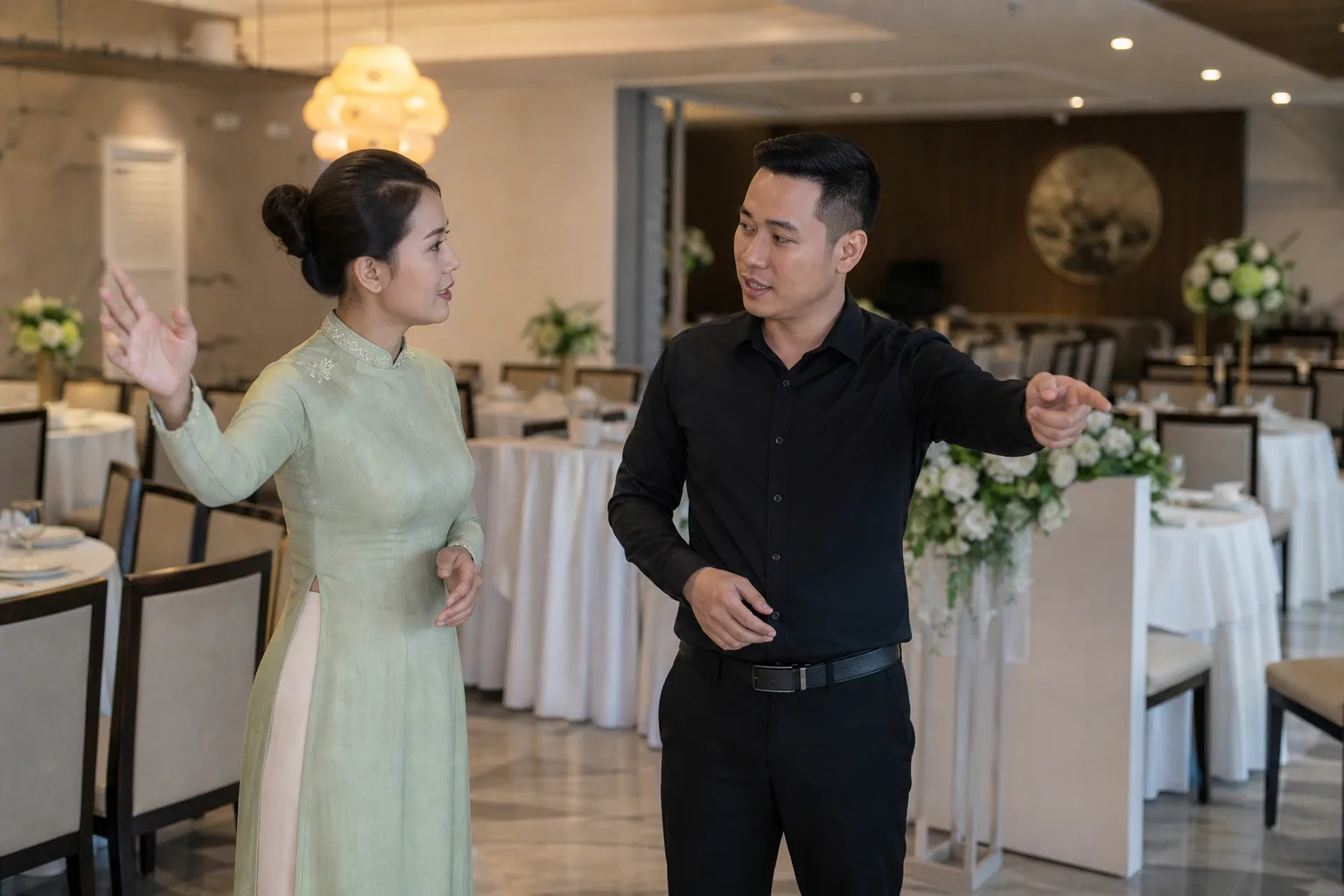 Người tổ chức sự kiện và nhân viên nhà hàng đang trao đổi ý tưởng bố trí khu vực trang trí trong không gian nhà hàng, thể hiện quá trình thống nhất nhu cầu trước khi triển khai.