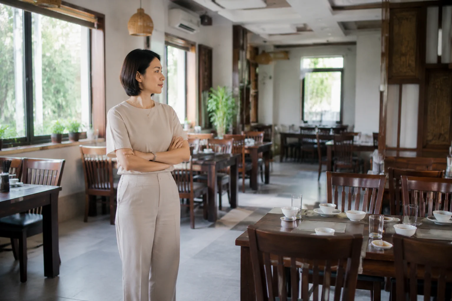 Người phụ nữ Việt Nam đứng quan sát bố cục bàn ghế và không gian phòng ăn trong nhà hàng, đánh giá sự phù hợp của khu vực trước khi quyết định đặt tiệc sinh nhật cho nhóm khách