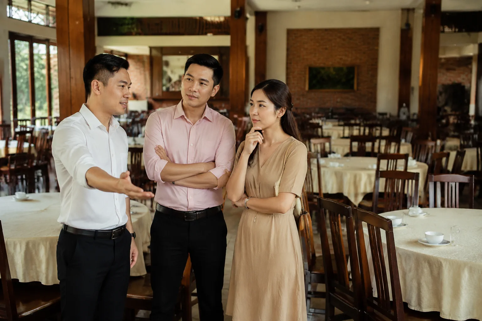 Nhân viên nhà hàng và cặp đôi Việt Nam trao đổi về cách sắp xếp bàn tiệc và khu vực phục vụ trong một góc không gian tiệc cưới, thể hiện việc ghi nhận thông tin sau khi khảo sát th